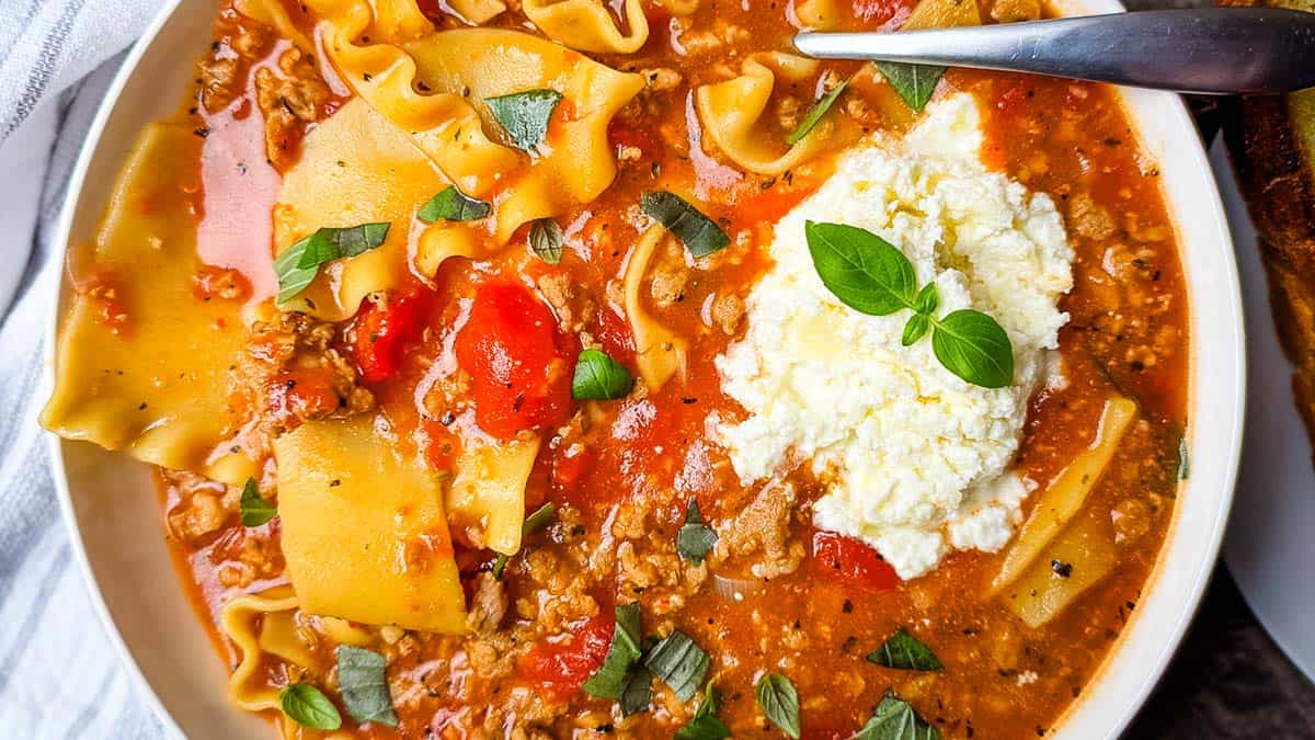 A hearty bull of thick and rich lasagna soup in a serving bowl, topped with fresh basil.