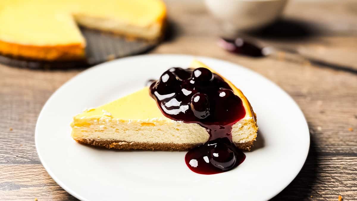 A slice of creamy smoked cheesecake topped with glossy blueberry sauce on a white plate.