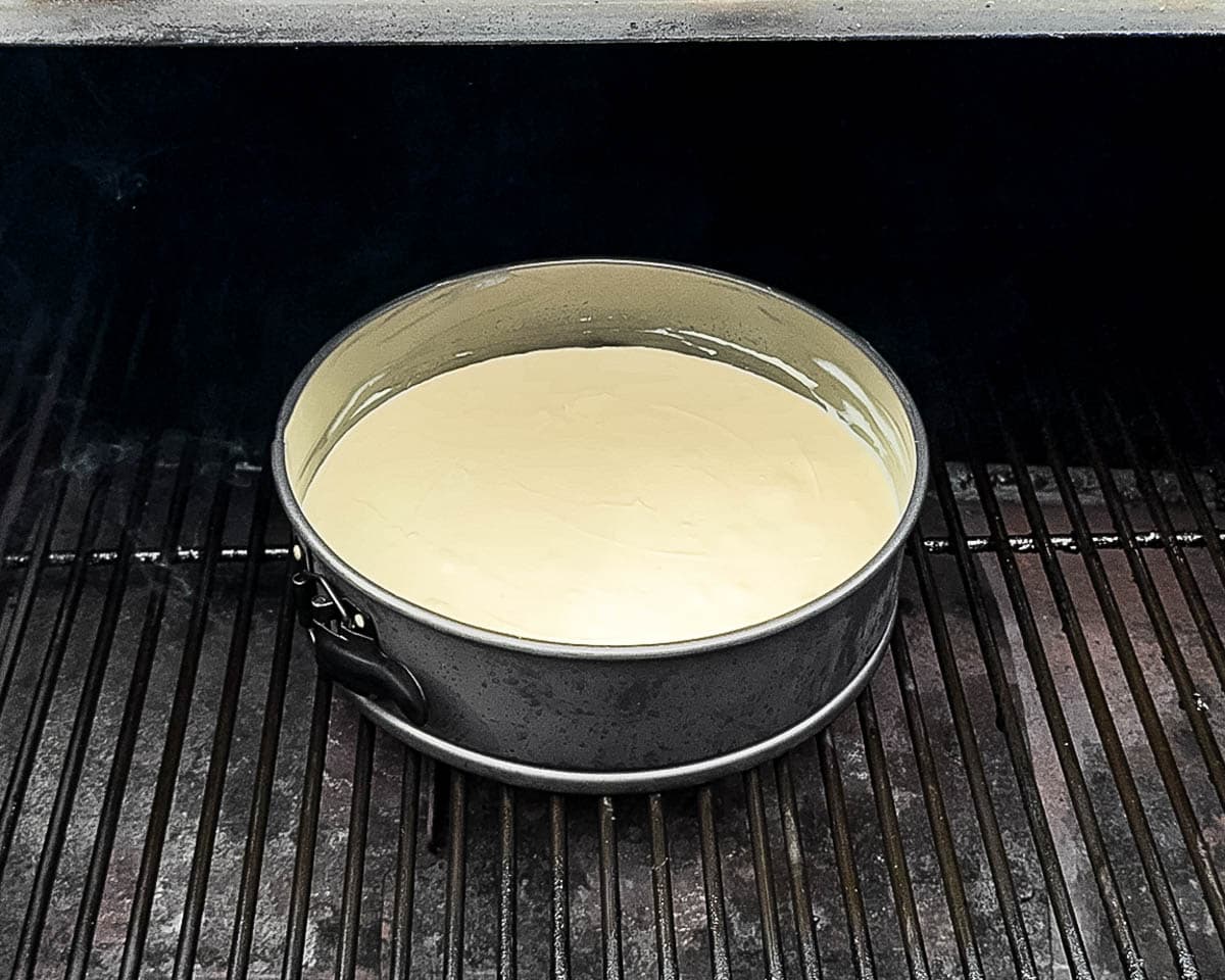 Unbaked cheesecake in a springform pan placed on smoker grates, ready to cook on a pellet grill.
