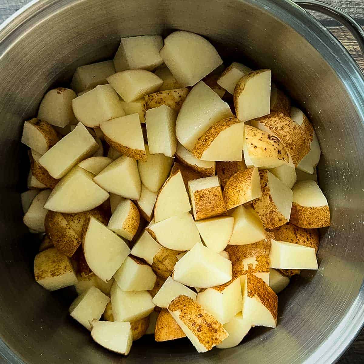 Unpeeled russet potatoes cut into chunks in a large pot, ready to be boiled for smoked mashed potatoes.