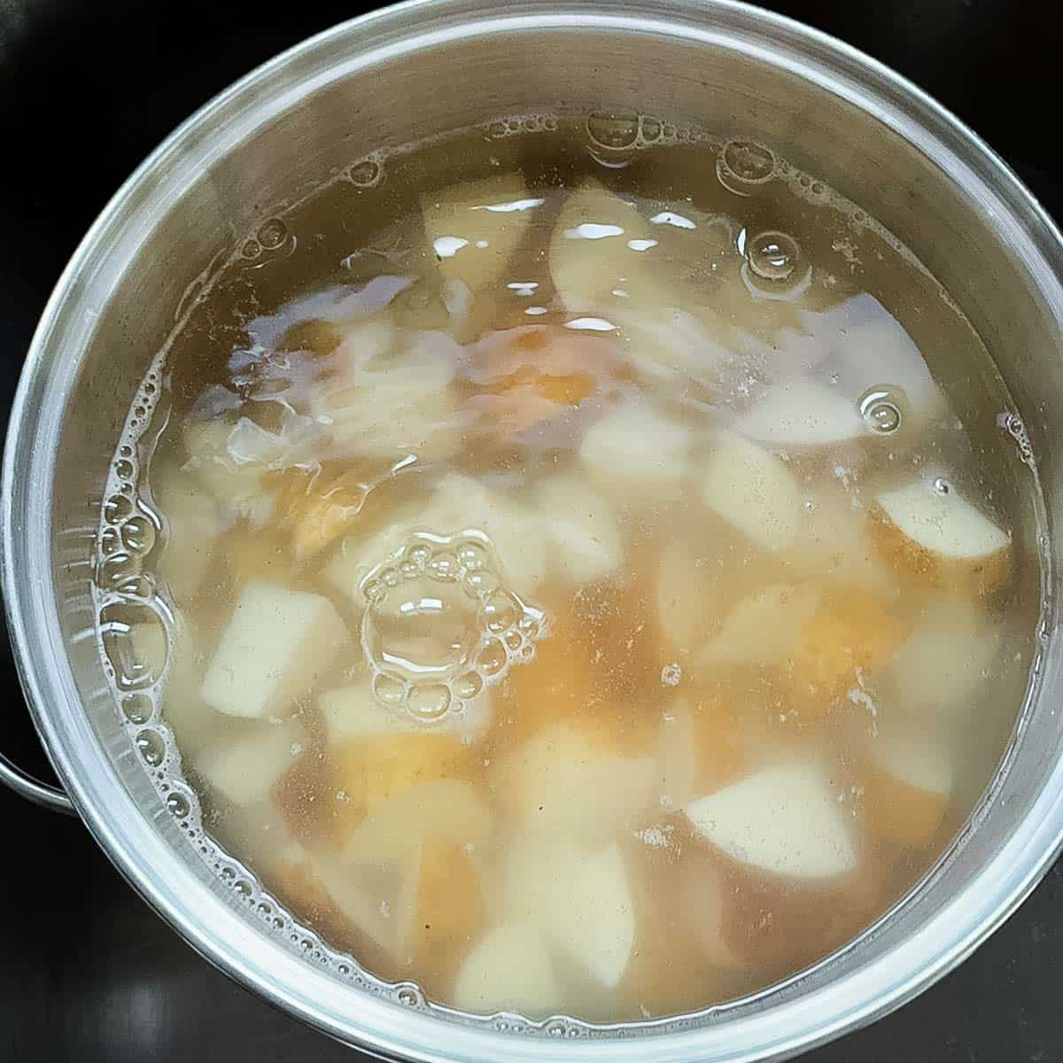 Potato chunks simmering in a large pot of water over medium heat until tender.