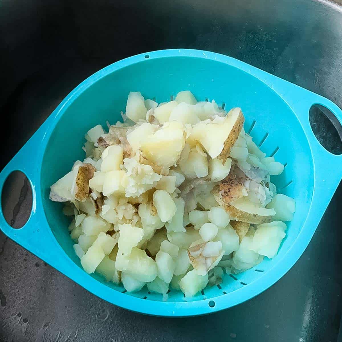 Cooked potatoes draining in a blue colander in the sink after boiling.