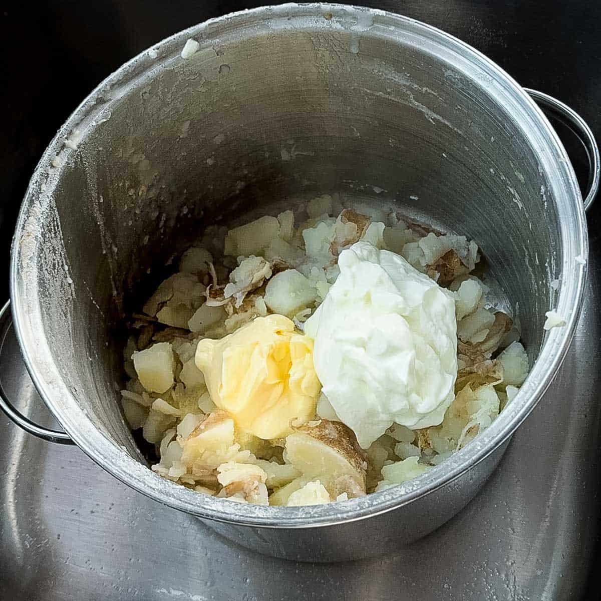 Boiled potatoes in a pot with butter and sour cream added, ready to mash.