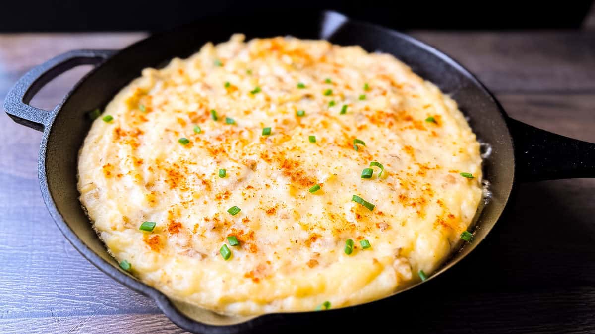 Close-up of creamy smoked mashed potatoes in a cast iron skillet, topped with paprika and chives, fresh off the pellet grill.