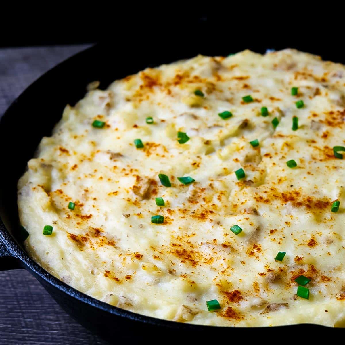 Close-up of creamy smoked mashed potatoes in a cast iron skillet, topped with paprika and chives, fresh off the pellet grill.