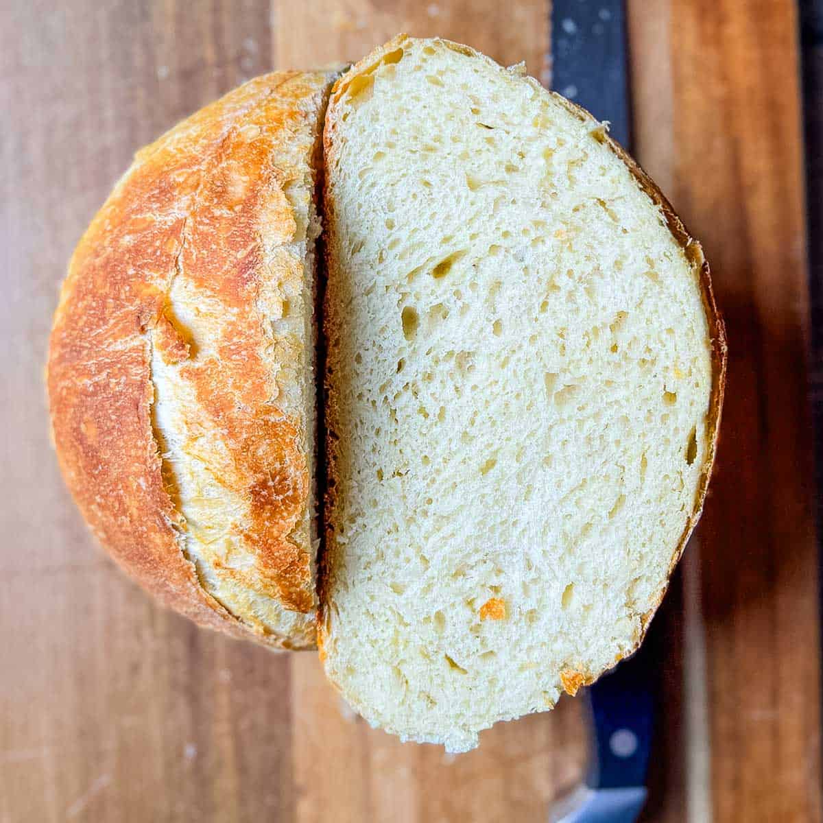 Freshly baked sourdough discard bread loaf sliced in half on a wooden cutting board, showing a soft, airy interior and golden crust.