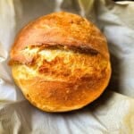 Rustic sourdough discard bread with a crisp golden crust and deep scoring, freshly baked in parchment paper.