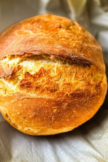 Rustic sourdough discard bread with a crisp golden crust and deep scoring, freshly baked in parchment paper.