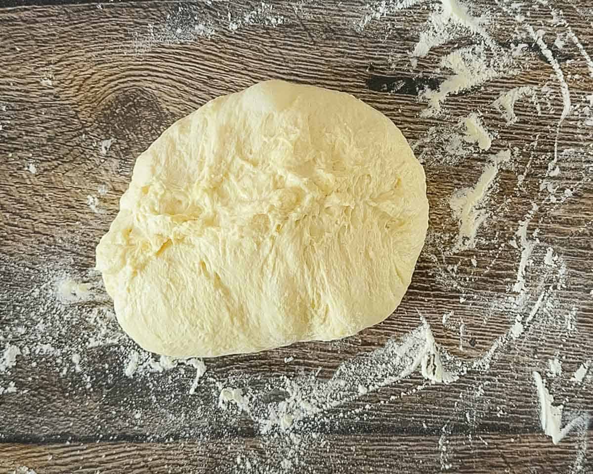 The bread dough on a wooden surface after the sides are pulled in and the seam pinched close.