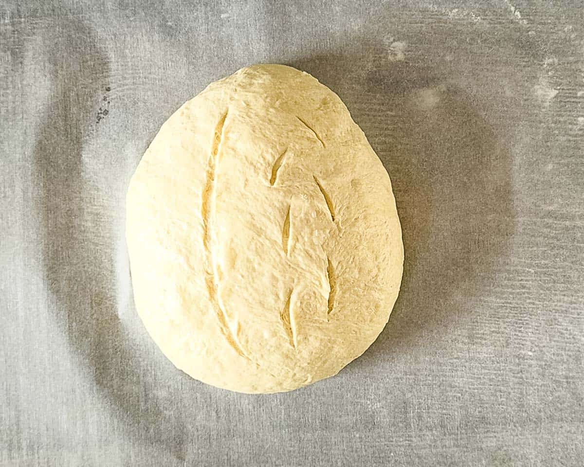 Shaped sourdough discard bread dough with decorative scoring lines on parchment paper, ready for the second rise.