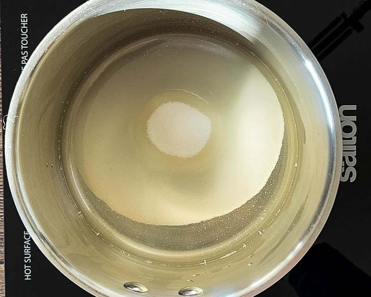 A saucepan filled with water and sugar heating on a stovetop, the first step in making homemade cranberry sauce.