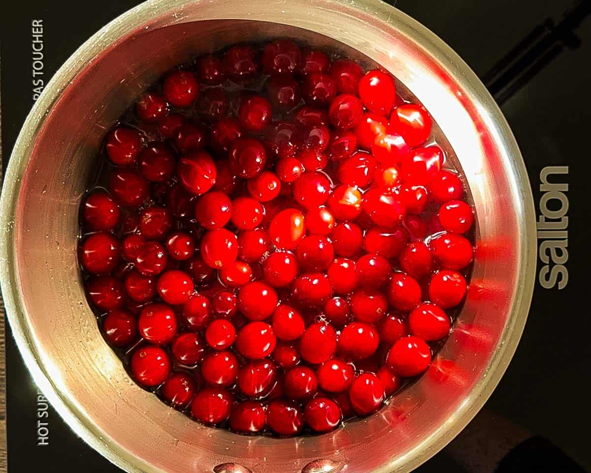Cranberries starting to simmer and burst in a saucepan as the sauce begins to thicken.