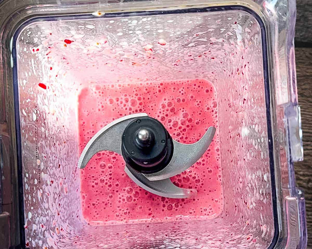 The bright pink cranberry smoothie fully blended in the blender, with small berry specks visible on the sides.