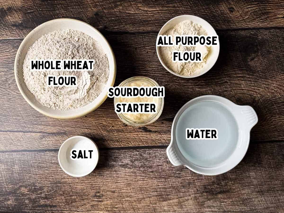 The labeled ingredients for homemade whole wheat sourdough bread on a rustic wooden table.