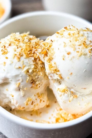 Two scoops of creamy Ninja Creami coconut ice cream in a white bowl, topped with toasted coconut flakes.