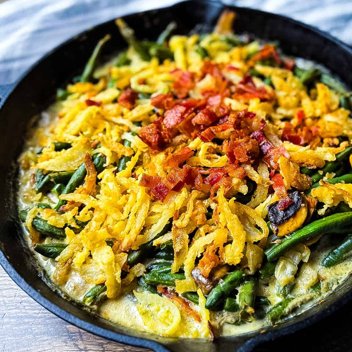 Creamy smoked green bean casserole topped with golden onions and chopped bacon in a cast iron skillet.