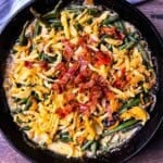 Smoked green bean casserole in a cast iron skillet topped with crispy onions and smoky bacon pieces.