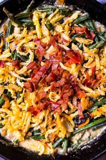 Smoked green bean casserole in a cast iron skillet topped with crispy onions and smoky bacon pieces.