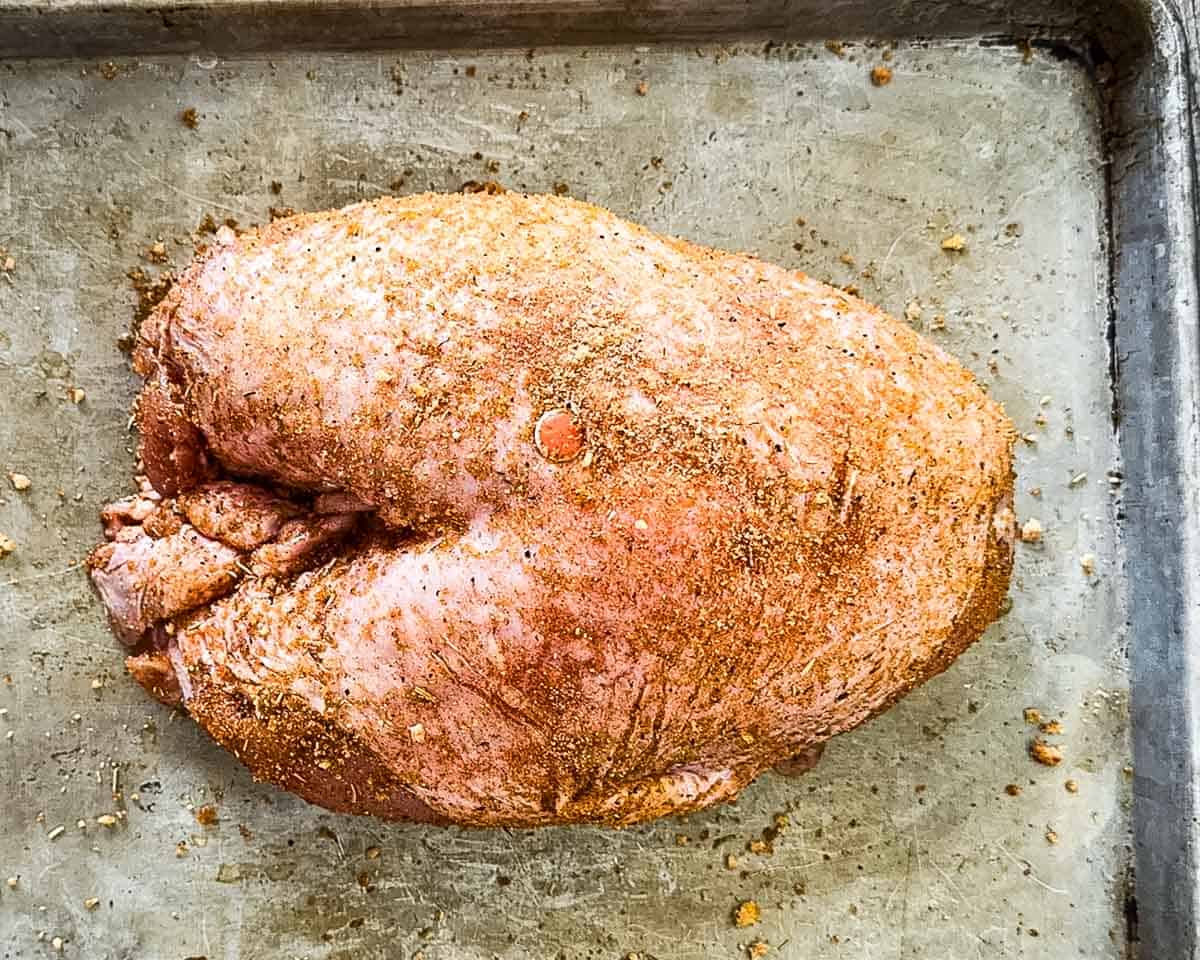 Bone-in turkey breast completely coated in homemade dry rub on a baking sheet, ready to be placed on the smoker.