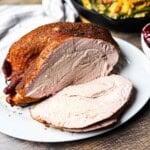 Golden brown smoked turkey roast sliced on a white plate, showing juicy, tender meat with a pink smoke ring.