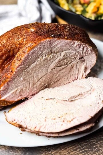 Golden brown smoked turkey roast sliced on a white plate, showing juicy, tender meat with a pink smoke ring.
