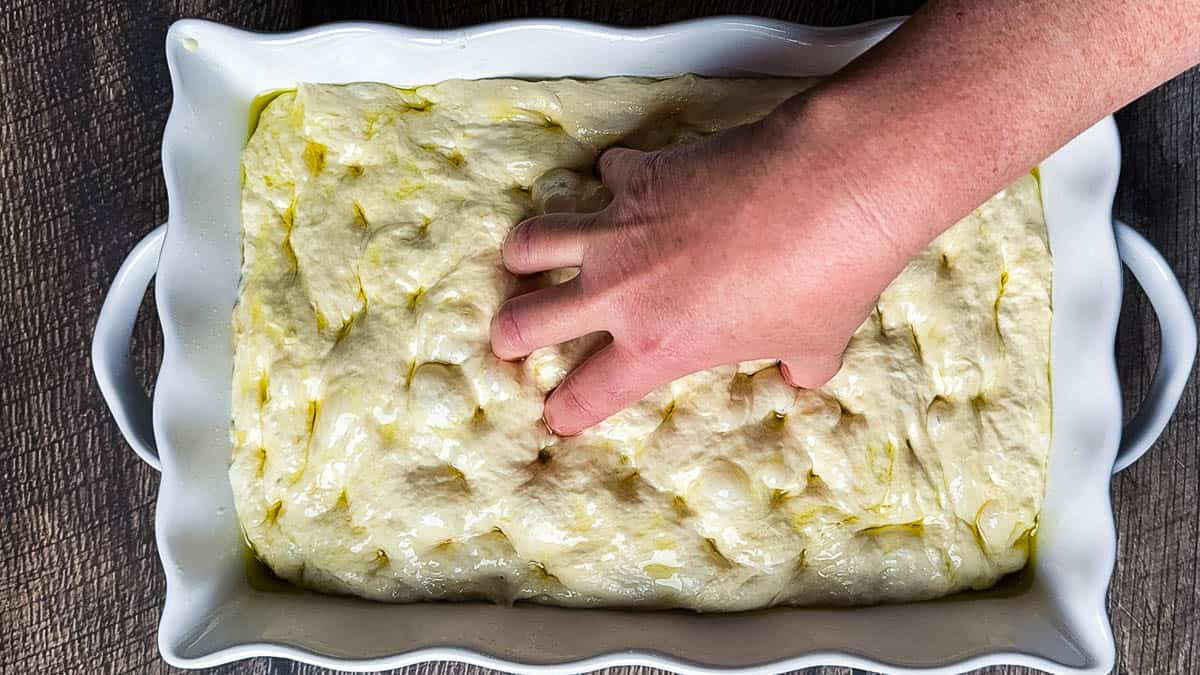 Jeri's hand making dimples in the focaccia dough.