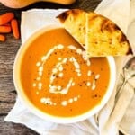 Bowl of roasted butternut squash soup with a swirl of cream, cracked black pepper, and warm flatbread on the side.