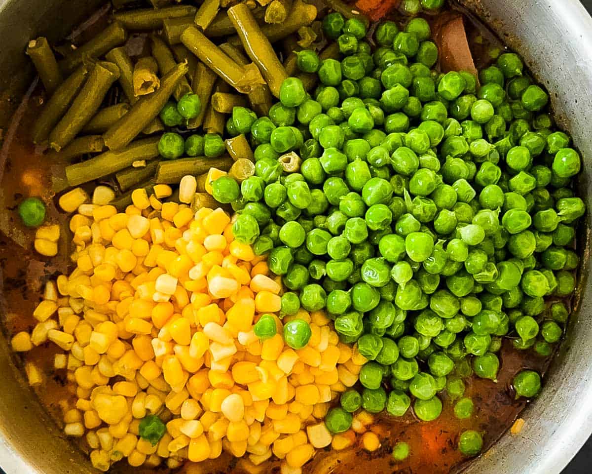 Green beans, corn, and frozen peas stirred into beef vegetable soup near the end of cooking.