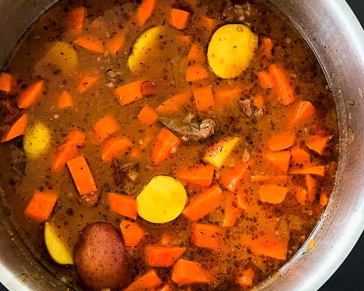 Beef vegetable soup simmering with carrots and potatoes until tender.