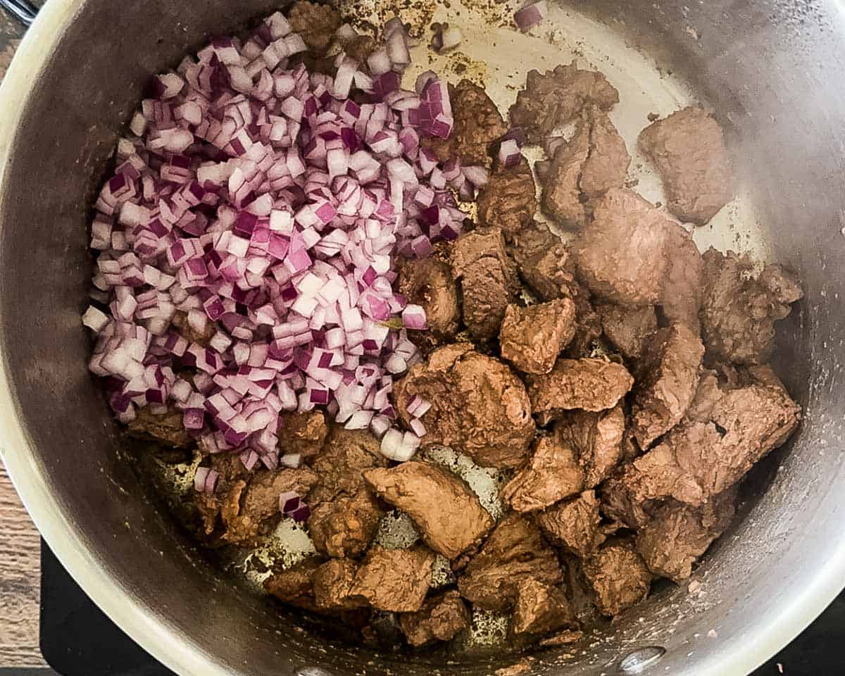 Chopped onion added to browned beef in a pot.