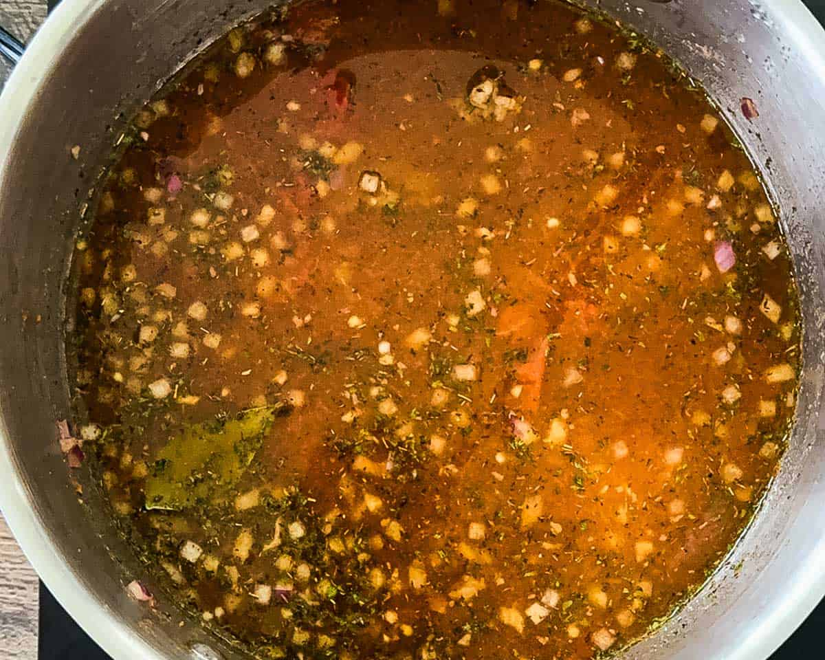 Beef vegetable soup beginning to simmer with broth, tomatoes, and seasonings in a large pot.