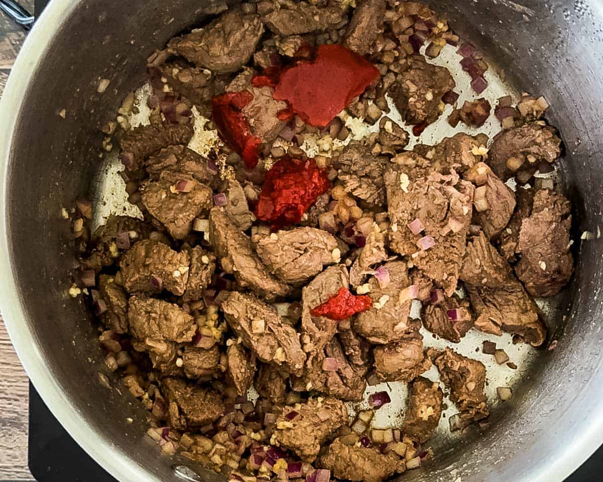 Garlic and tomato paste stirred into browned beef and onions to deepen flavor.