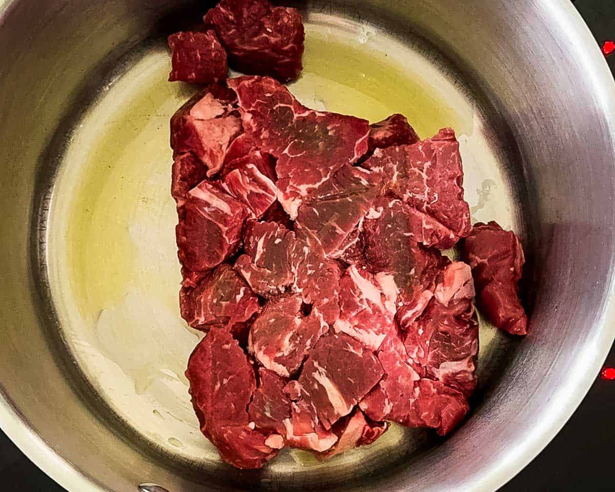 Raw beef chuck pieces added to a large pot with olive oil, ready to be browned for old-fashioned beef vegetable soup.