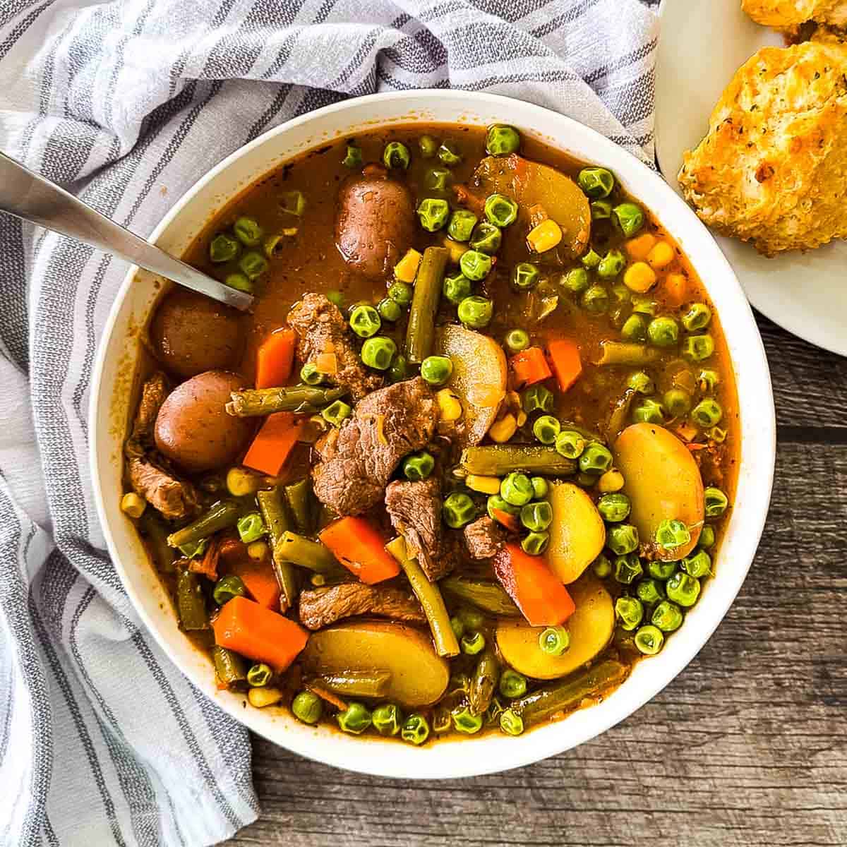 Old-fashioned beef vegetable soup with tender beef, potatoes, carrots, peas, and green beans in a rich broth, served in a white bowl.