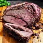 Slicing a juicy medium-rare smoked venison roast on a wooden cutting board.