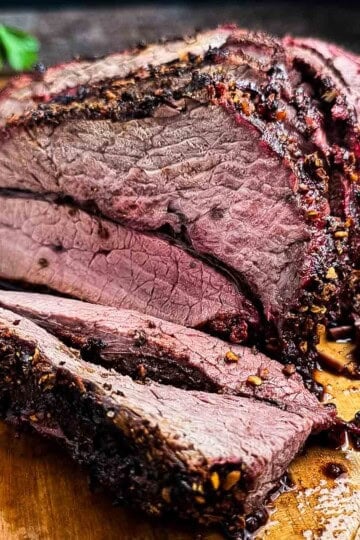 Slicing a juicy medium-rare smoked venison roast on a wooden cutting board.