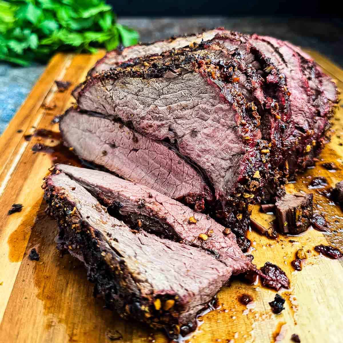 A sliced deer roast with flavored bark on a wooden cutting board.