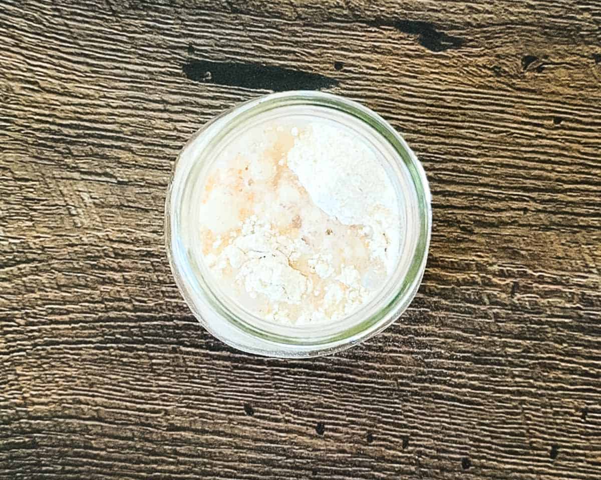 Whole wheat flour and water in a jar before stirring to create the initial sourdough starter mixture.