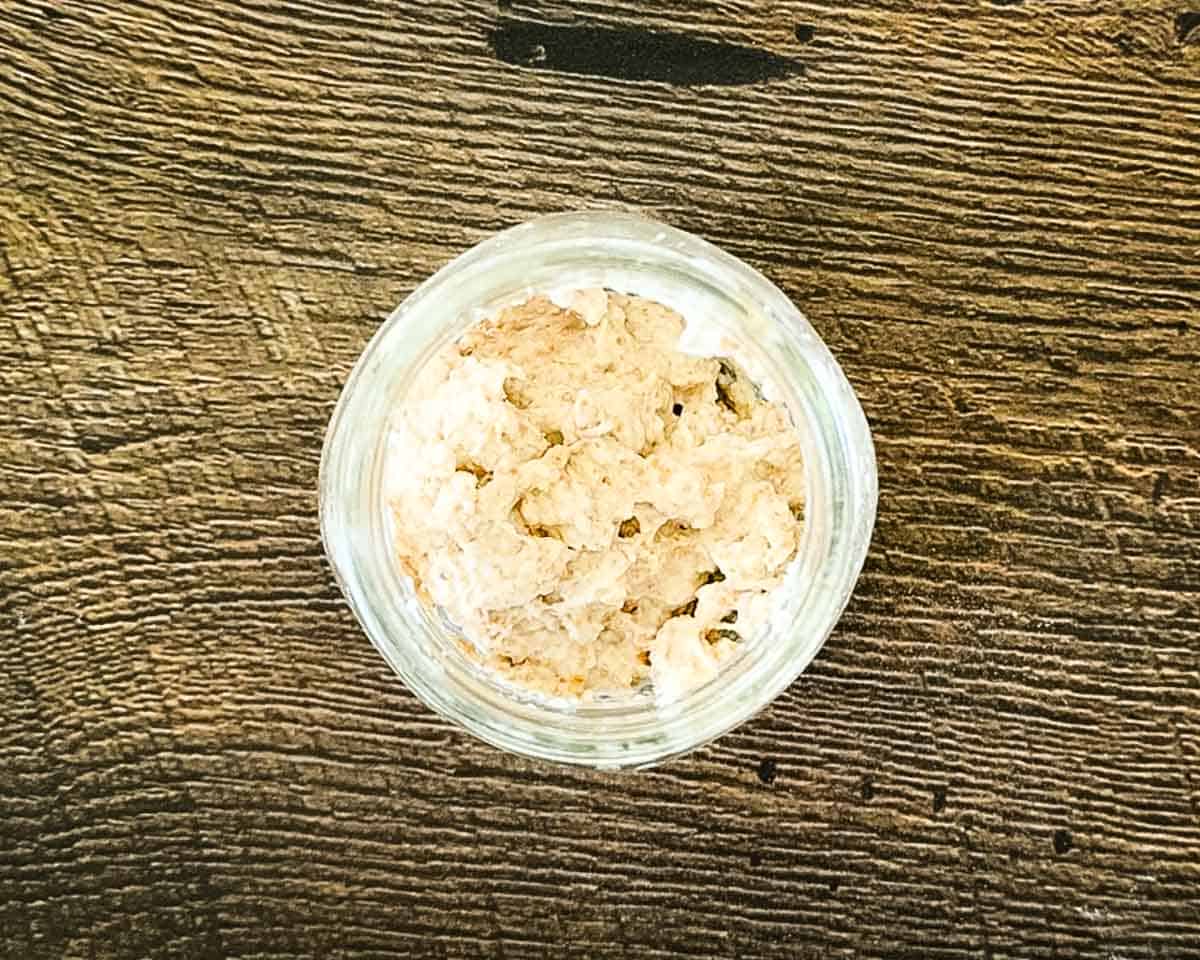 Day 1 sourdough starter mixture made with whole wheat flour and water, showing a thick, paste-like texture in a glass jar.