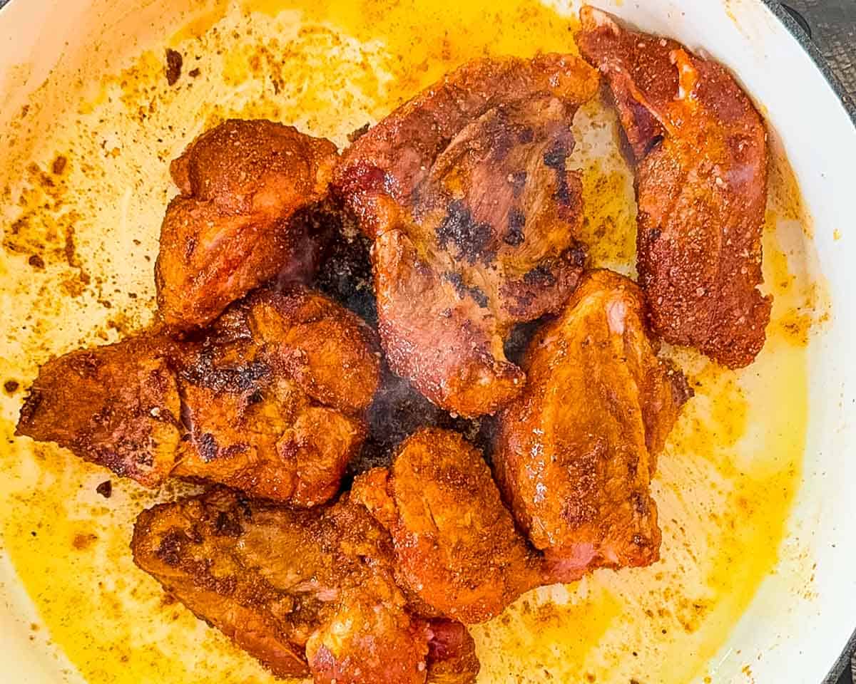 Pork shoulder pieces browned on all sides in a Dutch oven.