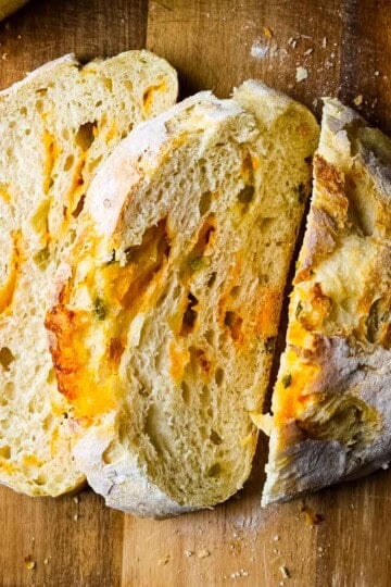 Sliced no knead jalapeño cheddar sourdough bread showing an airy crumb with melted cheddar and diced jalapeños throughout.