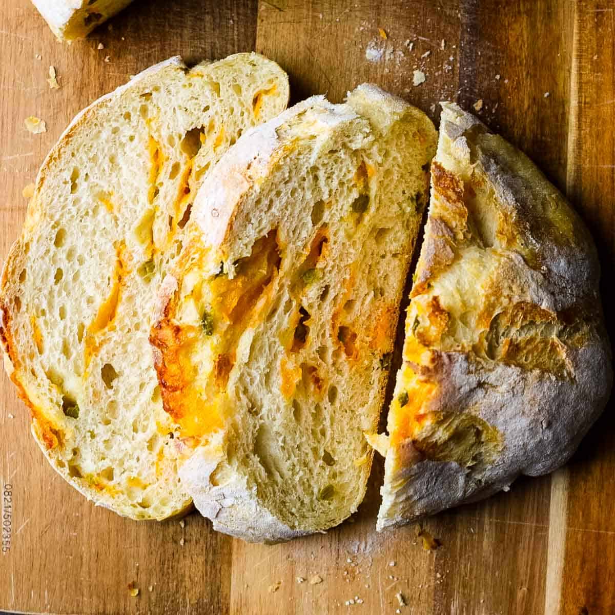 Sliced no knead jalapeño cheddar sourdough bread showing an airy crumb with melted cheddar and diced jalapeños throughout.