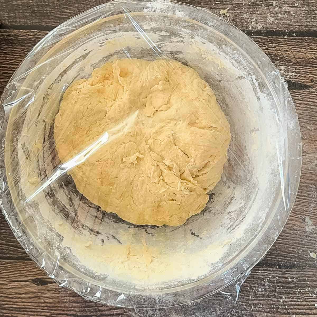 No knead sourdough dough after mixing, resting in a glass bowl covered with plastic wrap before bulk fermentation.