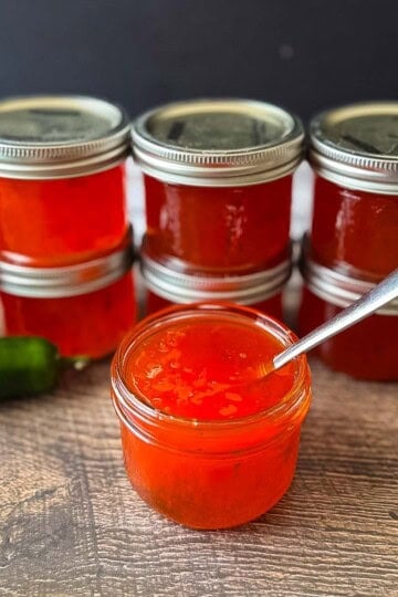Homemade red pepper jelly made with chopped peppers, shown in an open jar with sealed jars behind.