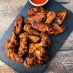 A platter of crispy Pit Boss smoked chicken wings with a golden brown dry rub, served with a side of dipping sauce.