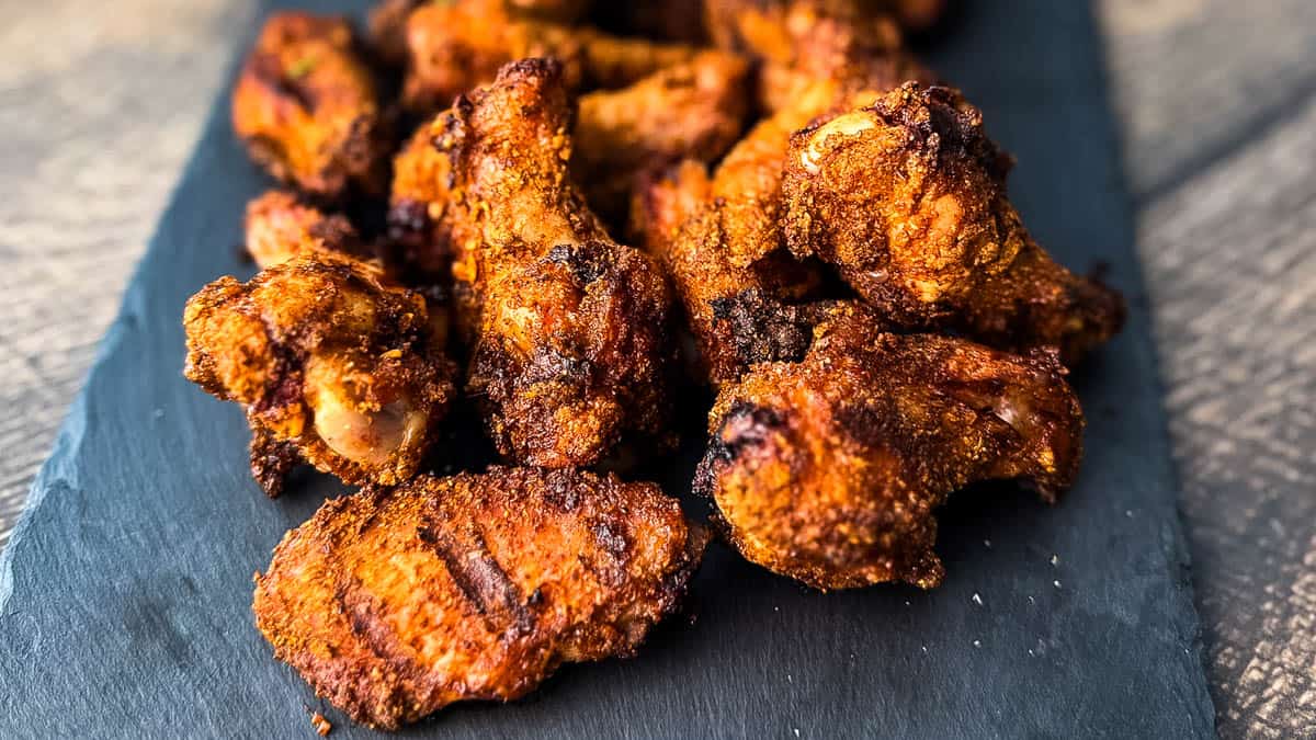 Crispy smoked chicken wings seasoned with dry rub and served on a slate board with dipping sauce, fresh off the pellet grill.