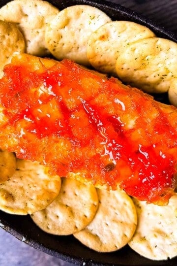 Smoked cream cheese in a cast iron skillet topped with red pepper jelly and surrounded by crackers.