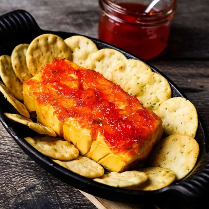Smoked cream cheese in a cast iron skillet topped with red pepper jelly and surrounded by crackers.