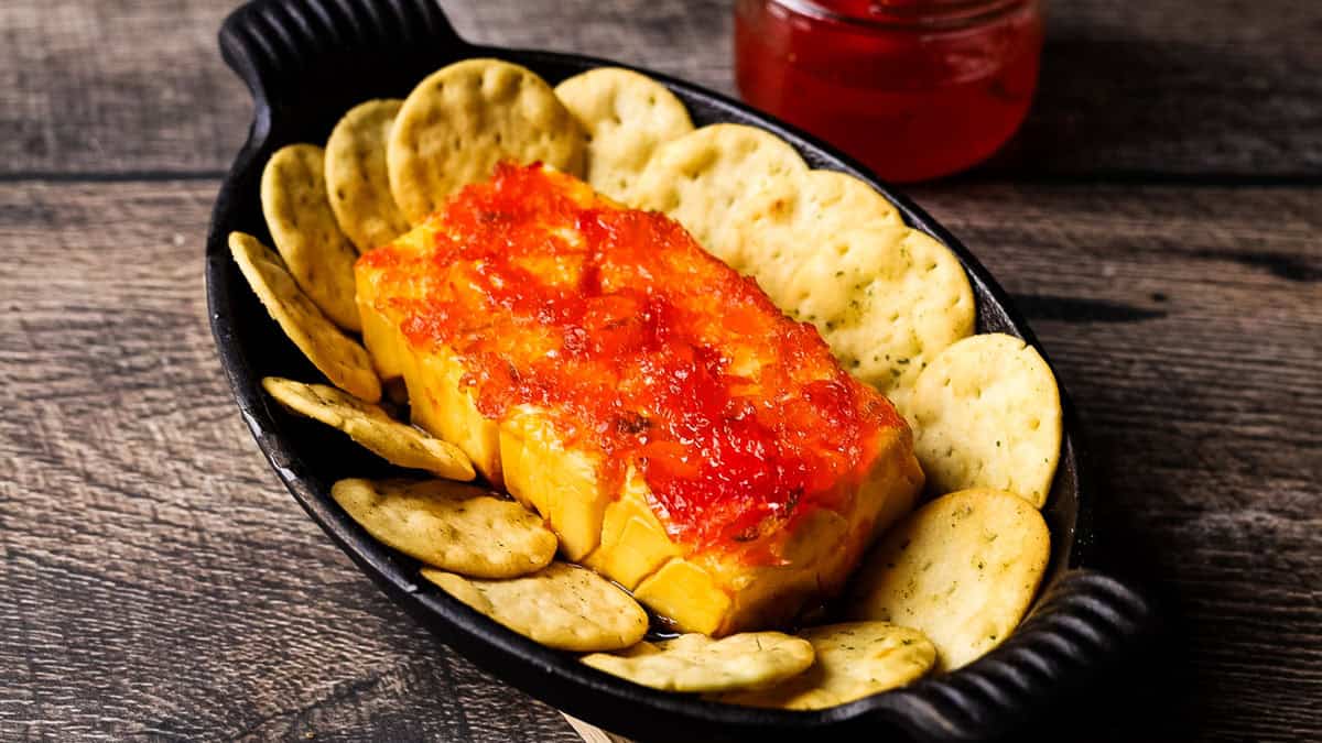 Smoked cream cheese topped with red pepper jelly in a cast iron skillet, with crackers for dipping.