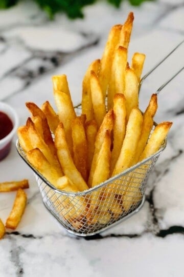 A mesh fry basket filled with golden brown, crispy air fryer frozen french fries.